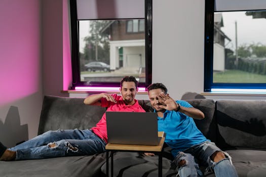 Two brothers sitting indoors, smiling as they engage in online learning on a laptop.